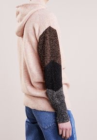 Hooded tröja i mjuk rosa med flerfärgade glittriga ärmar som har ett gradientmönster från brons till svart. Avslappnad passform, strukturerat material.