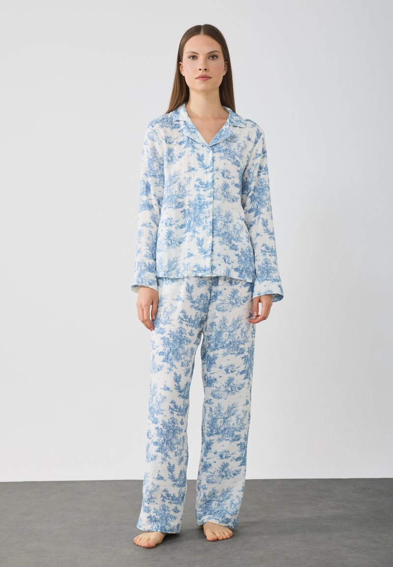 Blå och vit blommönstrad pyjamasuppsättning som består av en skjorta med knappar och långa ärmar samt matchande löst sittande byxor.