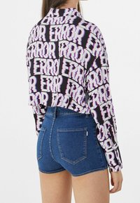 Cropped shirt in black with white and purple "ERROR" text pattern, paired with high-waisted blue denim shorts featuring back pockets.