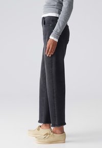 Jeans de mezclilla negros con un corte holgado, dobladillo desflecado y bolsillos traseros, combinados con zapatos estilo mocasín de color claro. Parte superior en gris.