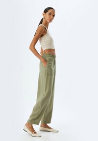 Licht olijfgroene linnen broek met brede pijpen, elastische tailleband en zijzakken, gecombineerd met een aansluitend beige geribd tanktop en crèmekleurige flats.