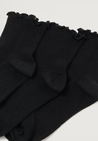 Μαύρες πλεκτές κάλτσες με ριγωτή υφή και φαρδιές μανσέτες. Ορατές τρία ζευγάρια, με ενιαίο χρώμα σε όλη την επιφάνεια.