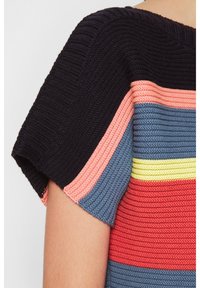 Gebreide top met korte mouwen in blokken in zwart, roze, blauw, geel en rood op de bovenarm en schouder van een persoon.