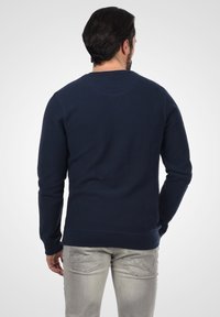 Mörkblå sweatshirt med långa ärmar, ribbat halsringning och manschetter, mjuk textur och rak nederkant; bärs över ljusgrå jeans.