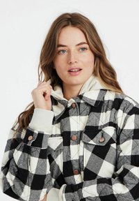 Geblokte gewatteerde jas van zwart-wit geruit stof, met een kraag, twee borstzakken en contrasterende crèmekleurige manchetten.