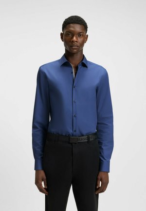 Blue long-sleeve shirt with a smooth texture and button closure. Worn with black trousers and a logo belt. Simple, fitted design.