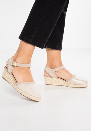 Beżowe koturny espadryle z fakturowaną górą z tkaniny, odkrytymi piętami i paskiem wokół kostki. Koturny owijane naturalnym sznurkiem dodają wysokości.