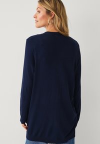 Marineblauw langemouwen shirt met een relaxte pasvorm, voorzien van een ronde halslijn en een zachte textuur. De achterkant is eenvoudig zonder patronen of accenten.
