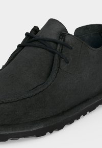 Μαύρο καστόρινη casual παπούτσι με ραφές moc toe και δερμάτινα κορδόνια σε μαύρη λαστιχένια σόλα πάνω σε λευκό φόντο.