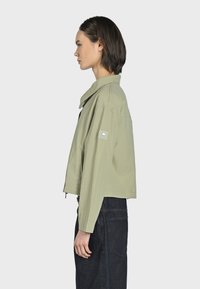 Ljusgrön kort jacka med bred krage, dragkedjestängning och sidofickor. Har en logotyp på vänster ärm.