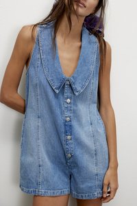 Ολόσωμη φόρμα από τζιν σε ανοιχτό μπλε, με μεγάλο γιακά, μπροστινά κουμπιά και κοντά μανίκια. Ομαλή υφή με εμφανείς λεπτομέρειες ραφής.