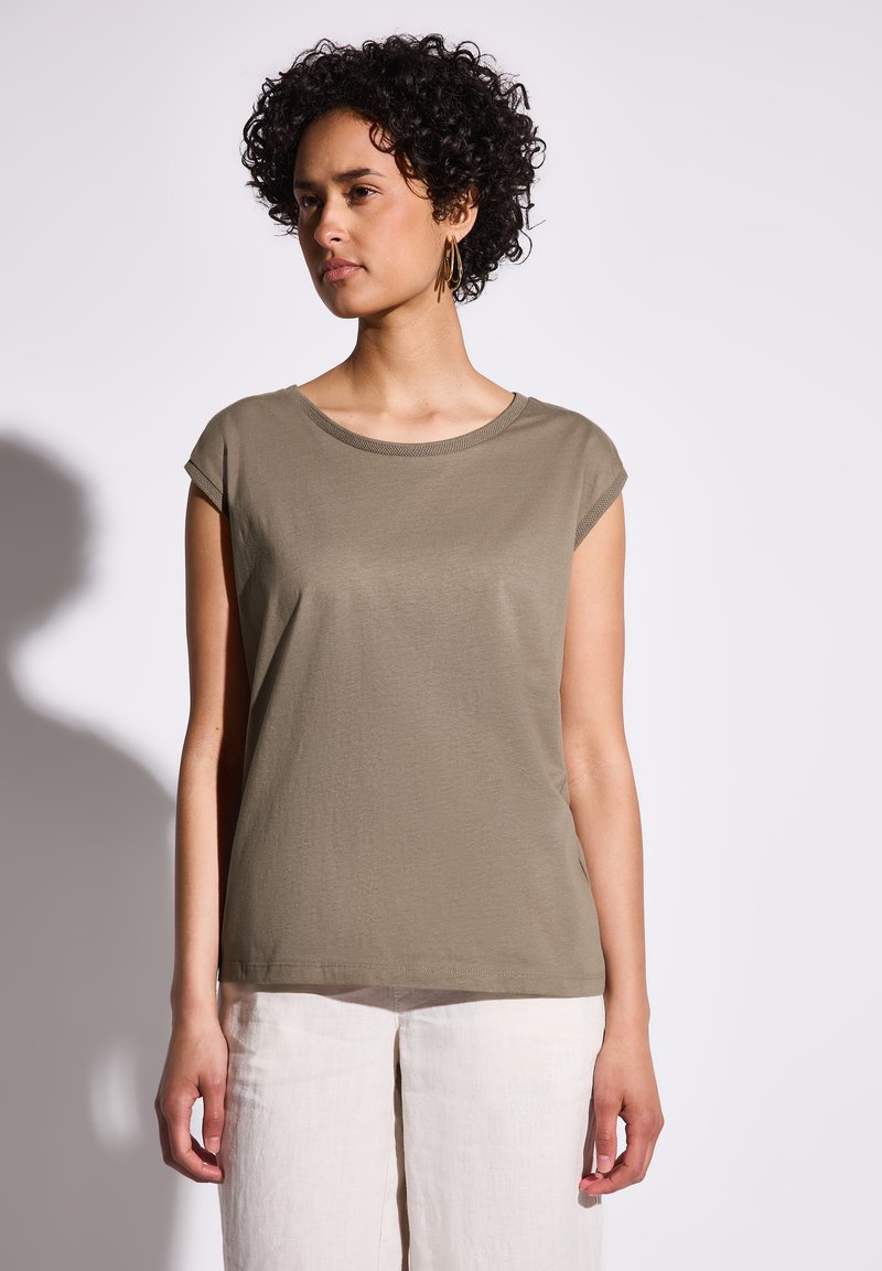 Maglietta verde oliva a maniche corte con scollo rotondo e texture liscia. Indossata con pantaloni di lino chiari, mostrando una vestibilità comoda.