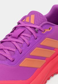 Fialová sportovní bota s růžovými akcenty. Texturovaný svršek, tkaničky a tři oranžové pruhy. Odolná gumová podrážka s vzorovaným dezénem.