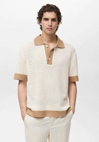 Tricou polo tricotat în crem cu un model texturat. Guler și manșete maro. Închidere cu două nasturi. Material ușor și respirabil.