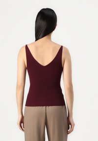 Top de tirantes finos en tono burdeos con canalé y espalda en V profunda, combinado con pantalones de pierna ancha en color marrón claro. Textura suave.