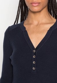 Pull en maille côtelée marine avec col en V, doté de cinq boutons sur le devant et d'une finition texturée. Conçu avec des manches longues.