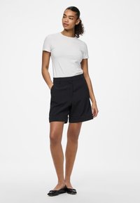 Bermudas pretas ajustadas com bainha dobrada, combinadas com uma t-shirt justa cinza-claro. Textura suave, corte clássico, adequado para uso casual.