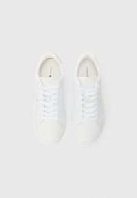 Par bijelih niskih tenisica s pertlama i suptilnim Tommy Hilfiger brandingom na bočnim stranama i ulošcima, pogledano odozgo na bijeloj pozadini.