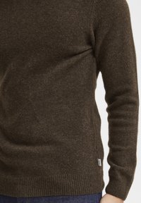 Pull en maille brun avec un col rond, des poignets et un ourlet côtelés. Texture douce, présente des fentes latérales et une petite étiquette à l'ourlet.