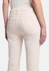 Jeans beige clair avec un design ajusté, des poches arrière et une texture lisse. Ils présentent des coutures subtiles et une taille haute.