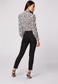 Un pantalon noir ajusté associé à un haut à fleurs avec des fleurs blanches et jaunes sur un fond noir. Silhouette élancée avec des manches longues.