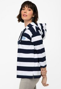 Pull à capuche rayé bleu marine et blanc, avec une fente sur le côté et un logo en accent bleu sur la poitrine. Tissu en coton, coupe décontractée.
