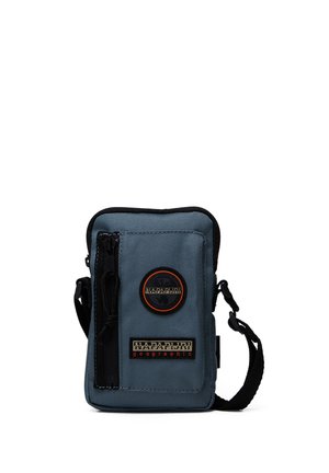 Blue fabric crossbody bag with zipper, adjustable strap, circular logo patch, and rectangular brand tag on front. Textured exterior.