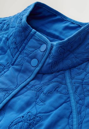 Niebieska pikowana kurtka z wysokim kołnierzem, zdobiona misternymi haftowanymi wzorami, dwoma niebieskimi zatrzaskami i teksturowaną tkaniną.