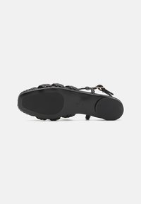 Svart sandal med vevd stroppedesign, flat såle og glatt tekstur. Har en sikker spenne og en holdbar gummisåle.