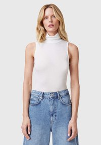 Top blanco de cuello alto con textura acanalada, hecho de un material elástico, con diseño sin mangas y un ajuste ceñido, combinado con jeans azul de cintura alta.