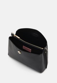 Czarna skórzana torebka o gładkiej fakturze, z magnetycznym zapięciem, kieszenią na zamek błyskawiczny oraz kontrastowym wnętrzem. Widoczna metka Coccinelle.