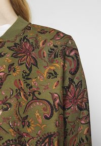 Bomullströja i olivgrönt med blommigt och paisleymönster i rosa, guld och svart. Ribbad krage och mjuk textur.