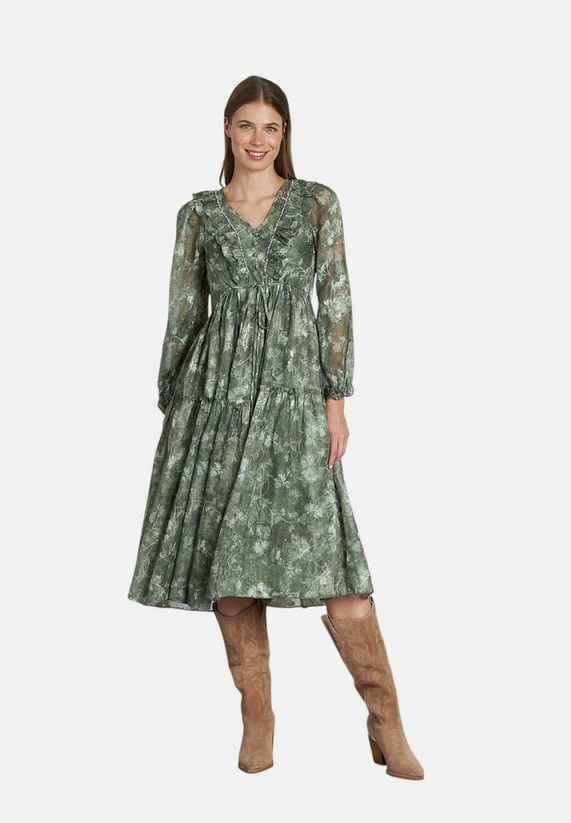Vestido midi floral verde con escote en V, volantes y mangas largas de gasa. Estilizado con botas altas color tostado. Tejido texturizado, diseño en capas.