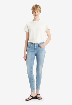 Light blue skinny jeans with a high waist, made of denim, paired with a cream-colored cotton t-shirt and black strappy sandals.