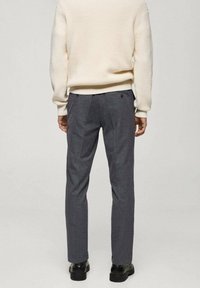 Pantaloni grigi scuri da uomo su misura con una finitura testurizzata, dotati di una tasca posteriore singola e un taglio aderente. Indossati con un maglione lavorato a maglia color crema.