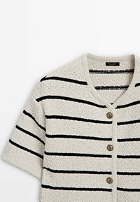 Cardigan tricoté à manches courtes avec des rayures horizontales noires sur fond beige et trois boutons décoratifs sur le devant.