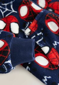 Niebieska tkanina polarowa z czerwonym nadrukiem Spider-Mana i białymi akcentami; posiada żebrowany granatowy mankiet; miękka tekstura z wzorami pajęczej sieci.