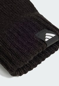 Black knitted glove with ribbed texture, featuring a white brand logo tag on the cuff, emphasizing durability and practical design.
