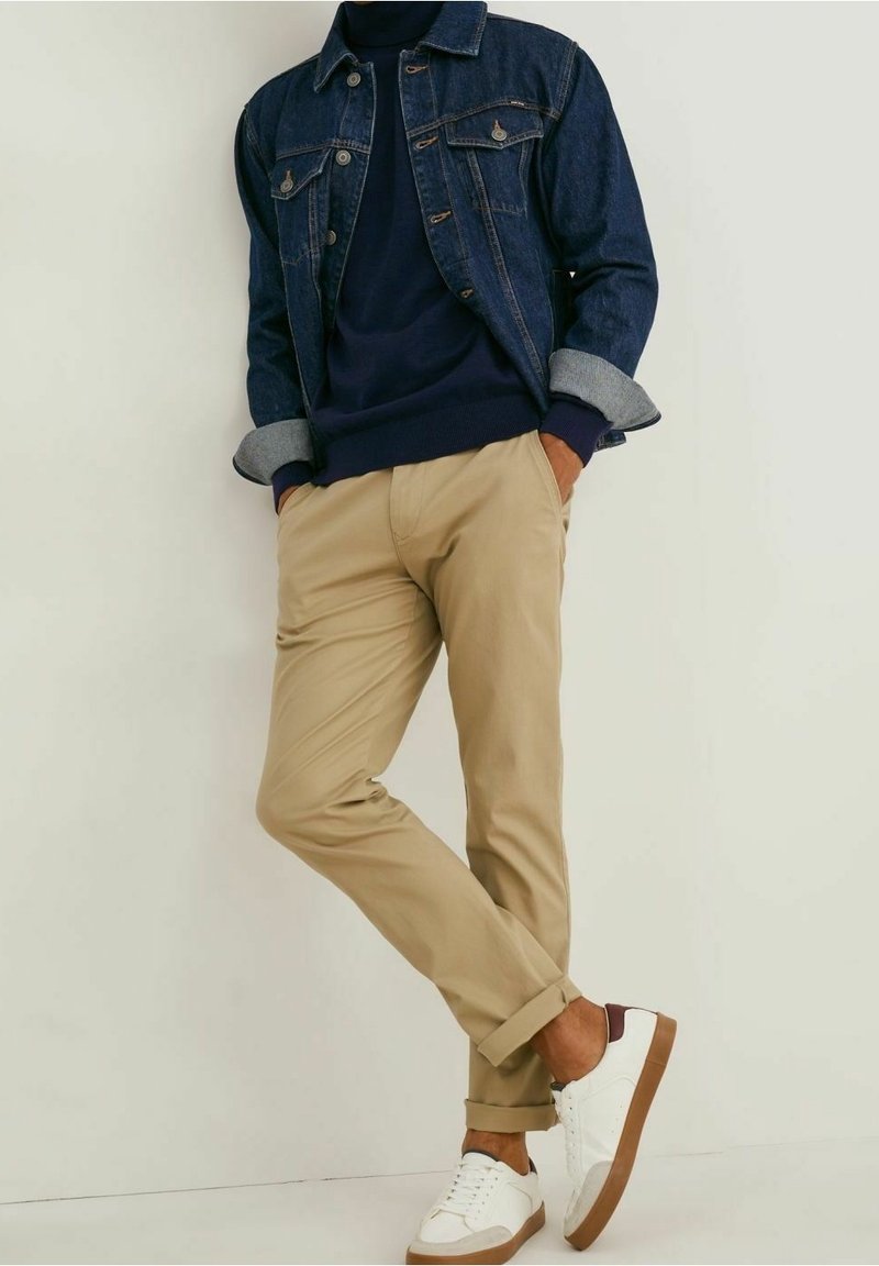 Jeansjacka, marinblå tröja, khakifärgade chinos och vita sneakers med bruna detaljer. Uppkavlade ärmar och byxben ger textur och kontrast.