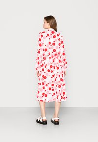Vestido de manga longa, até aos joelhos, em branco com um padrão floral que apresenta flores vermelhas e rosas. Usado com sandálias de plataforma pretas.