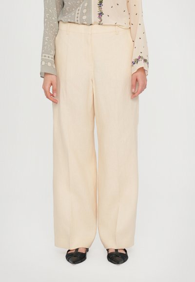 Pantaloni a gamba larga in lino beige chiaro, caratterizzati da una superficie liscia e un design pulito. Abbinati a sandali neri con cinturini.
