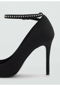 Chaussure à talon haut noire avec une texture lisse et mate, dotée d'une bride de cheville ornée de strass transparents. Profil à talon aiguille.