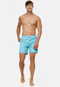 Helleblaue Badeshorts aus glattem Material, mit einem Kordelzugbund, Seitentaschen und einem kontrastierenden schwarzen Etikett am Bein.