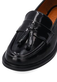 Zwarte gepatineerde leren loafers met een slank ontwerp, ronde neus en kwastaccent op een gestructureerde bovenkant. Vlakke zool voor stabiliteit.