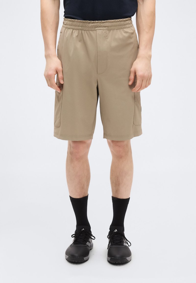 Χακί σορτς με ελαστική μέση, διαθέτοντας πλαϊνές τσέπες και λεία, ελαφριά υφή. Φοριέται με μαύρες κάλτσες και παπούτσια.