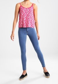 Débardeur floral rose avec des fines bretelles, associé à un jean skinny bleu et des espadrilles noires. Tissu lisse et design ajusté.