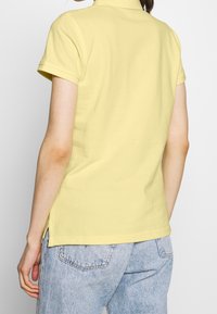 Polo shirt jaune avec une coupe ajustée, des manches courtes, un col et des fentes latérales, associé à un jean en denim bleu clair.