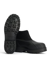 Mustat kumiset ja mokkanahkasaappaat, joissa on teksturoitu, karkea pohja, jossa on ristikkäismalleja. Sileä päällyspinta, jossa on vahvistettu varvas- ja nilkkakappale.