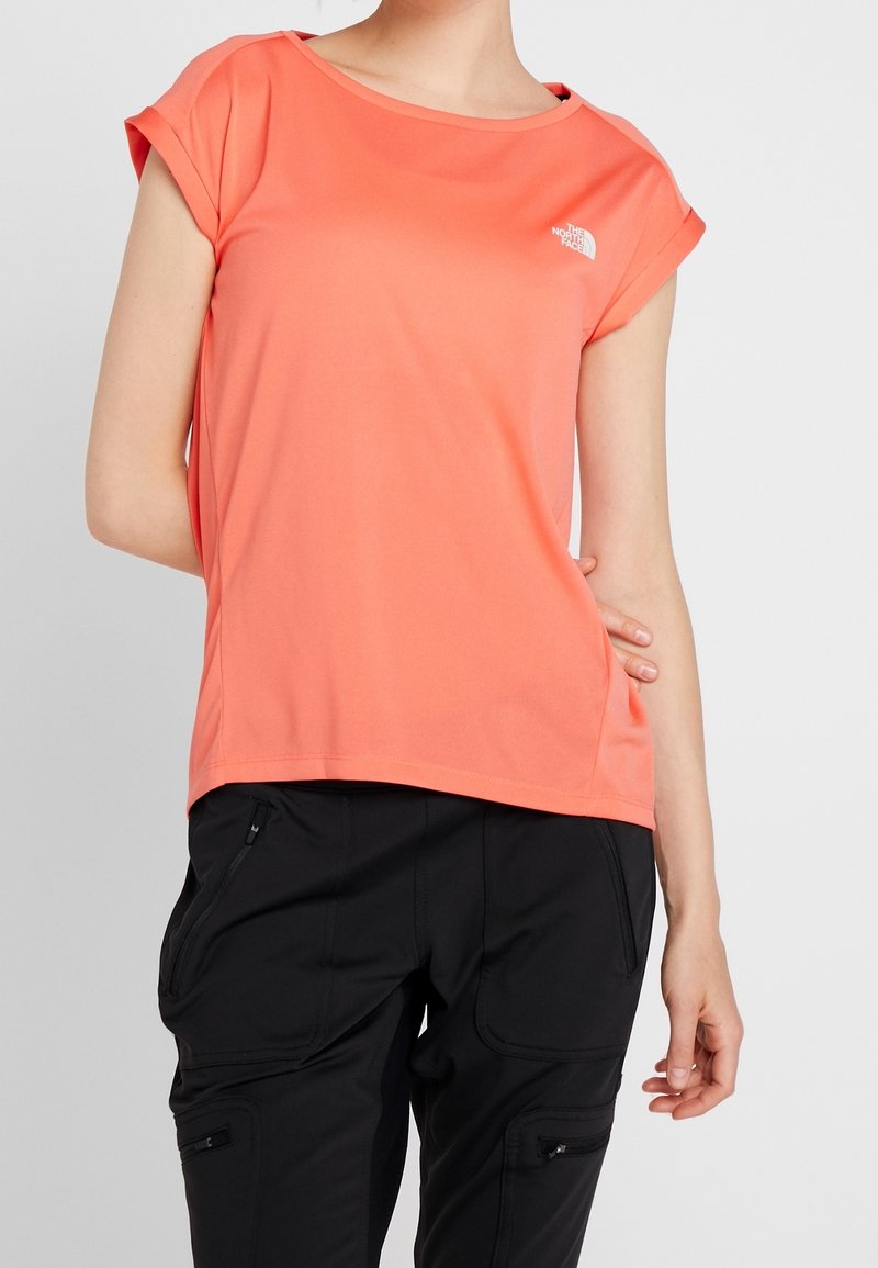 Korálové tričko s krátkým rukávem vyrobené z měkké látky, s kulatým výstřihem a logem na hrudníku. V kombinaci s černými cargo kalhotami.