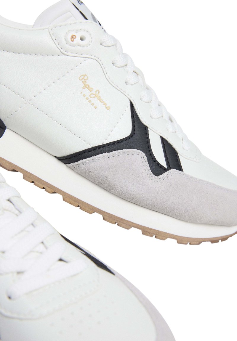 Zapatillas deportivas blancas con acentos en negro y gris, que presentan una parte superior de cuero y ante, cordones y una suela de goma con una superficie texturizada.